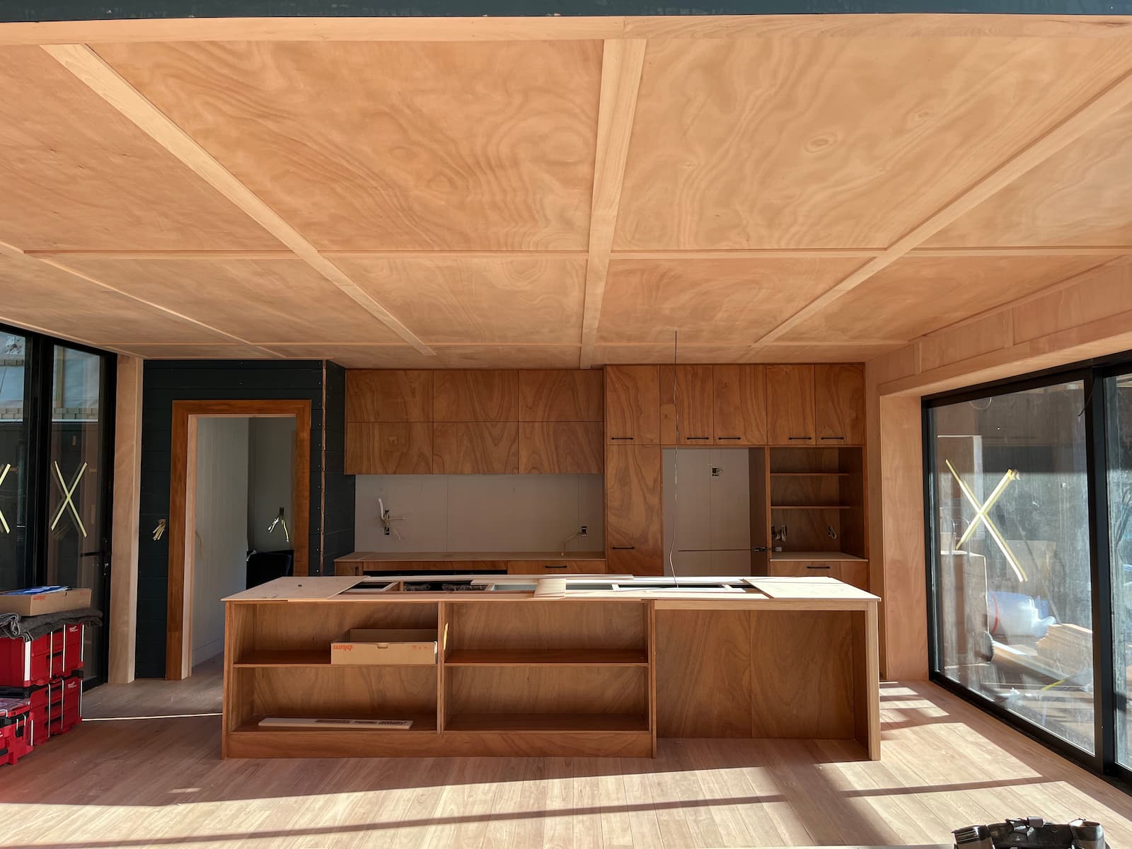 Modern kitchen and living area with gaboon board and batten ceiling and custom gaboon plywood cabinetry in a new Auckland build by Macalister Construction.