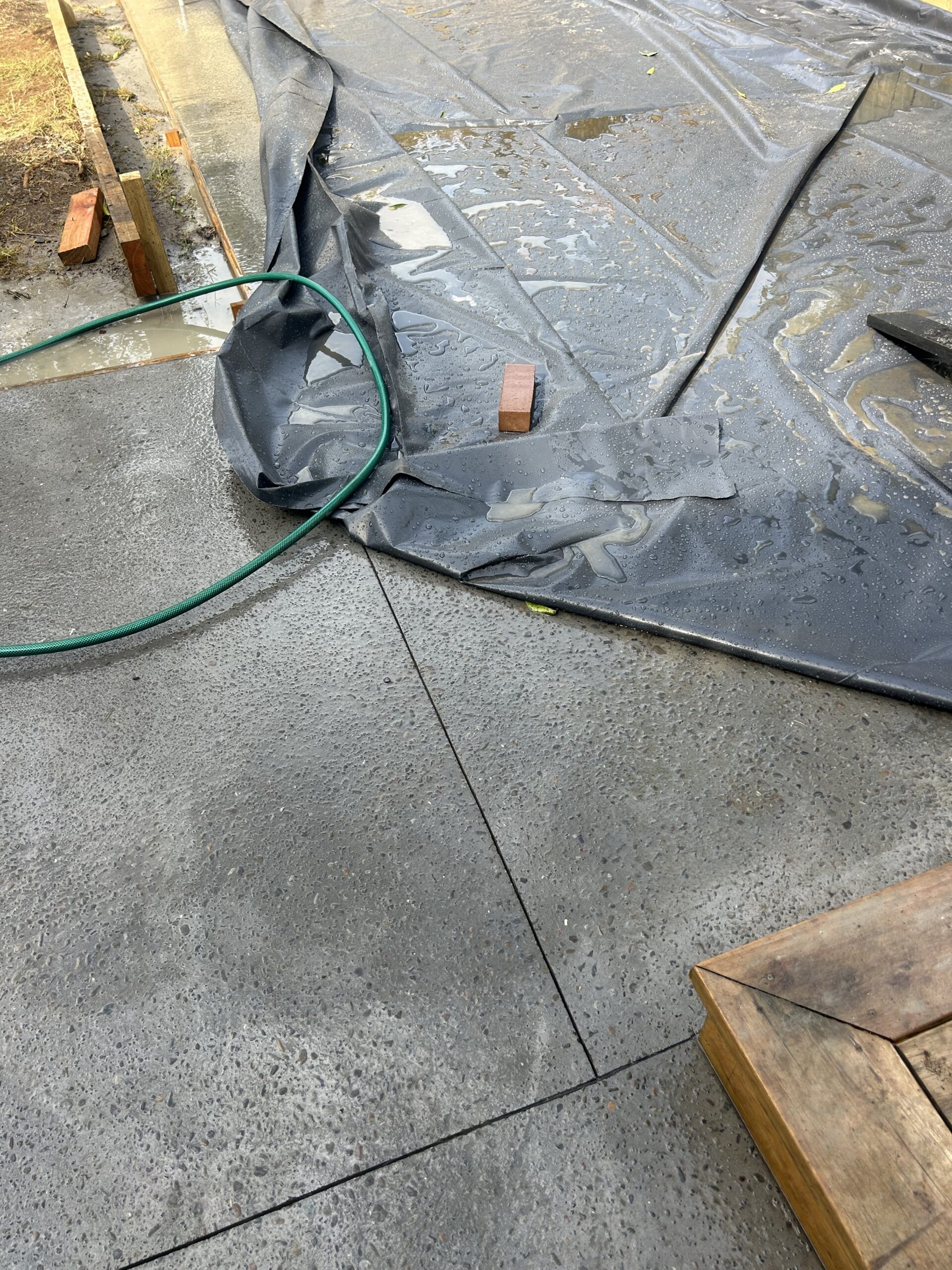 Exposed aggregate concrete patio curing under tarpaulin with control joints at internal corner Mt Eden Auckland