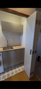 Custom laundry renovation featuring full-height concertina doors, timber benchtop, subway tile splashback and patterned floor tiles in an Auckland home.